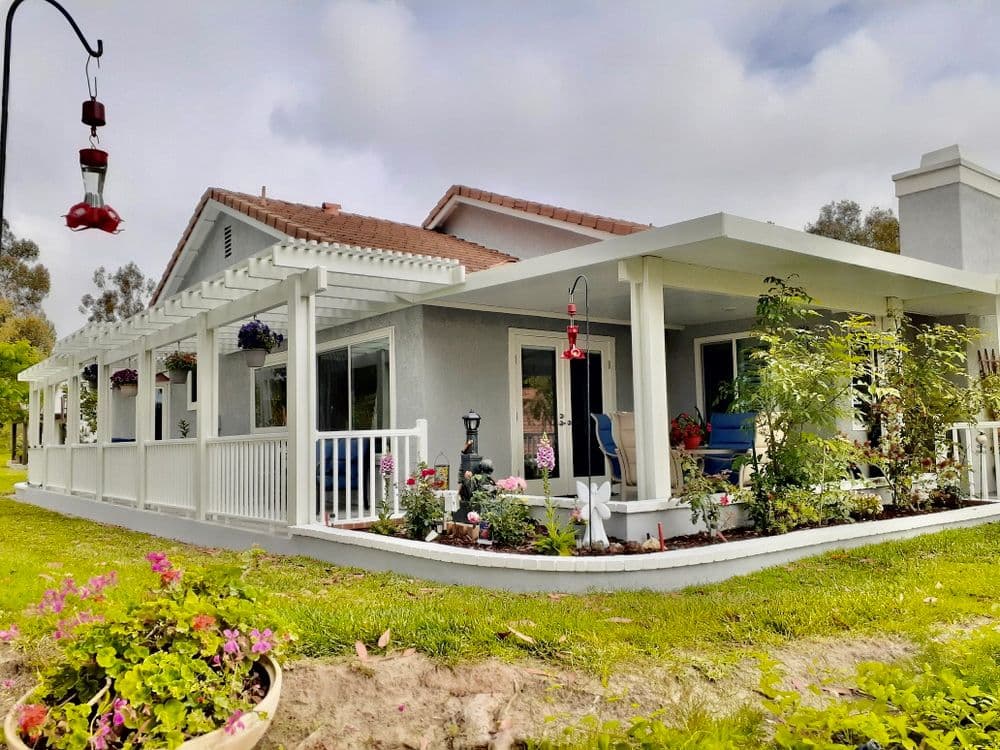 Charming house with a white porch, colorful flowers, and hummingbird feeder in a green garden.