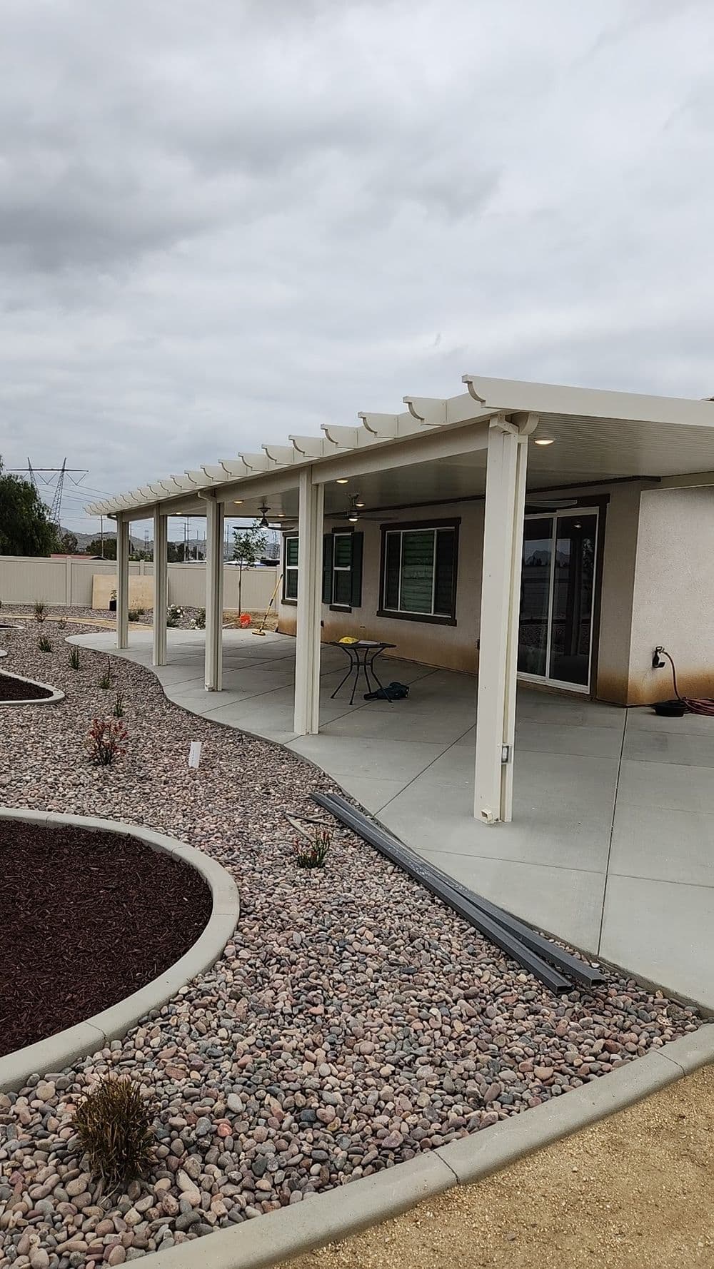 Modern outdoor patio with pergola and landscaped gravel garden. Cloudy sky in background.