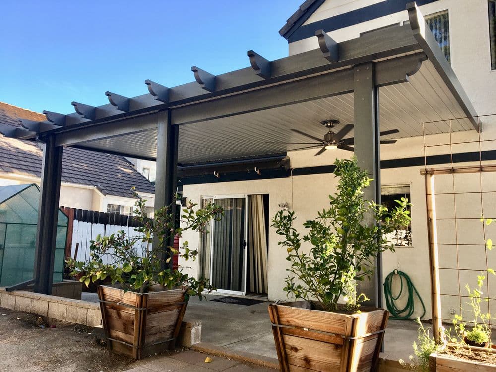 Modern patio featuring pergola, ceiling fan, and wooden planters with greenery.