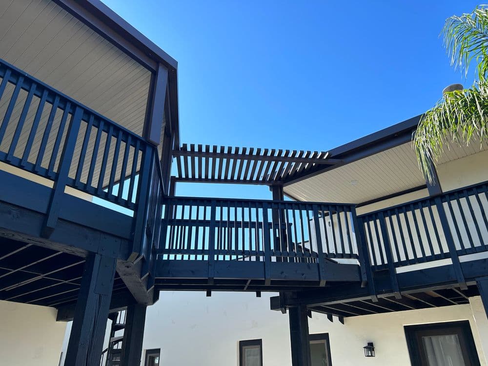 Black wooden deck with a pergola and clear blue sky in the background.