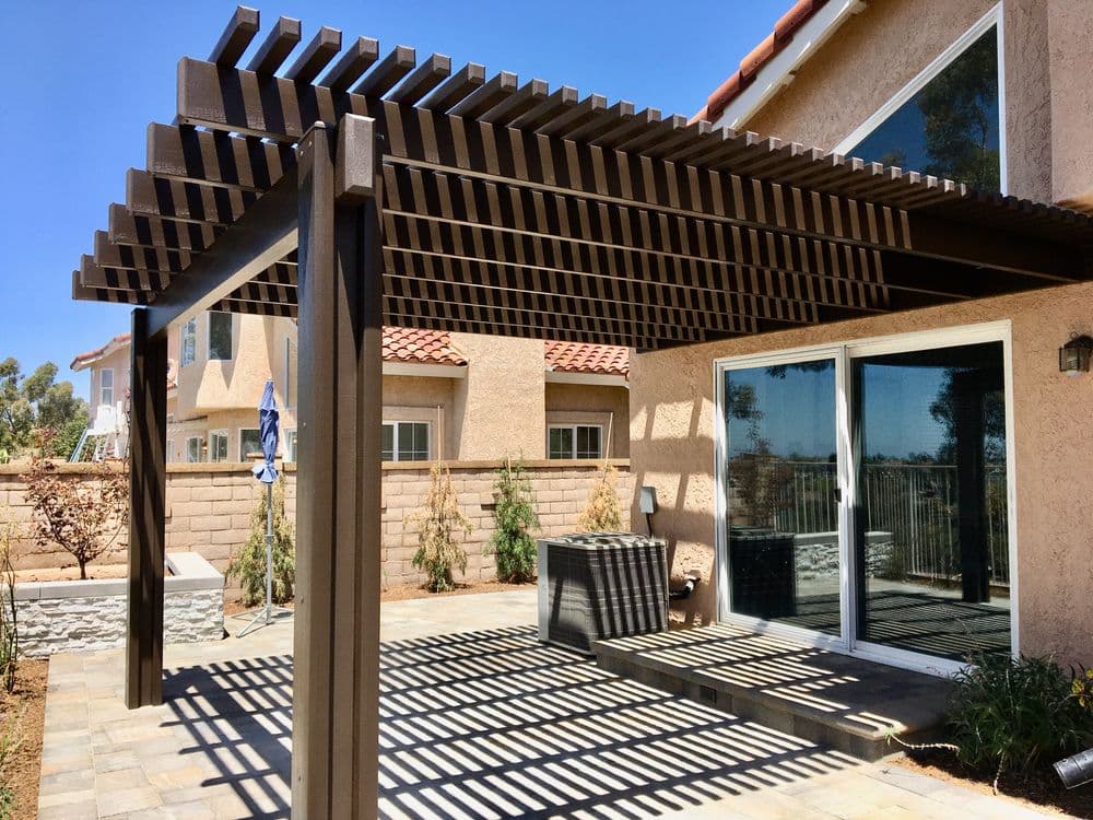Backyard patio with a pergola, stone pavers, and a view of nearby homes under a clear blue sky.