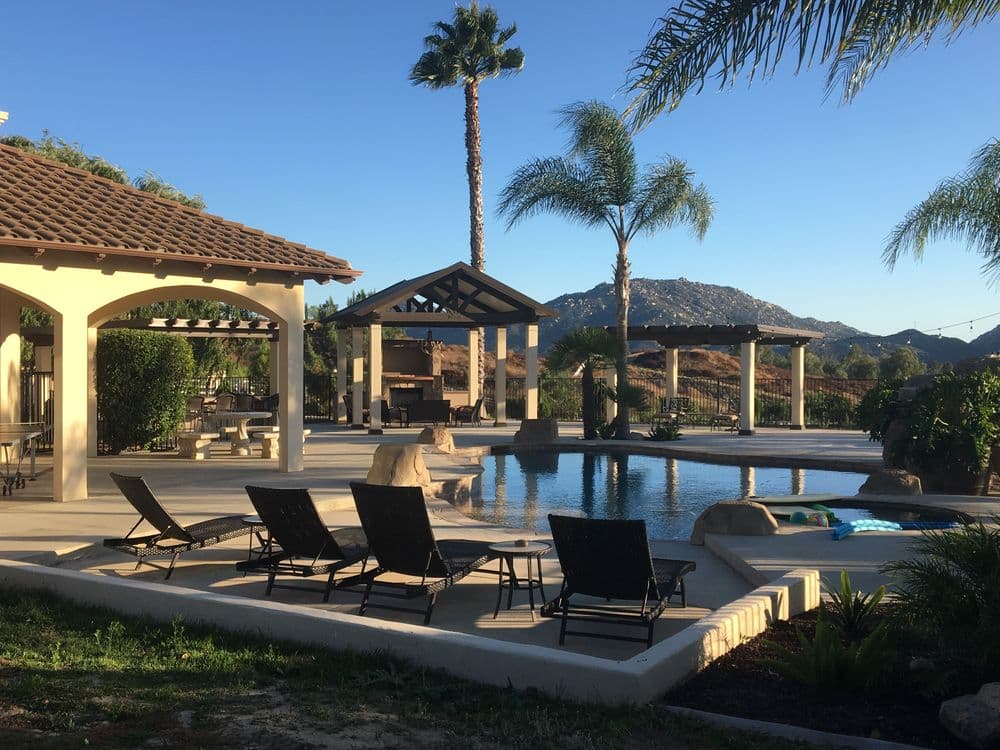 Luxury outdoor pool area with lounge chairs, palm trees, and mountains in the background.
