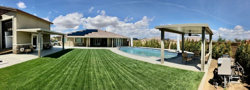 Panoramic view of a well-maintained backyard with a swimming pool, grass, and covered patio.